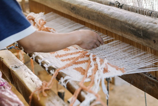 Indigenous artisan hand weaving a wool rug with a foot loom.